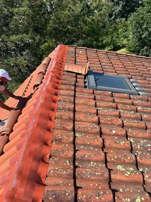 Couvreur au travail à côté d'une fenêtre de toit en cours de pose